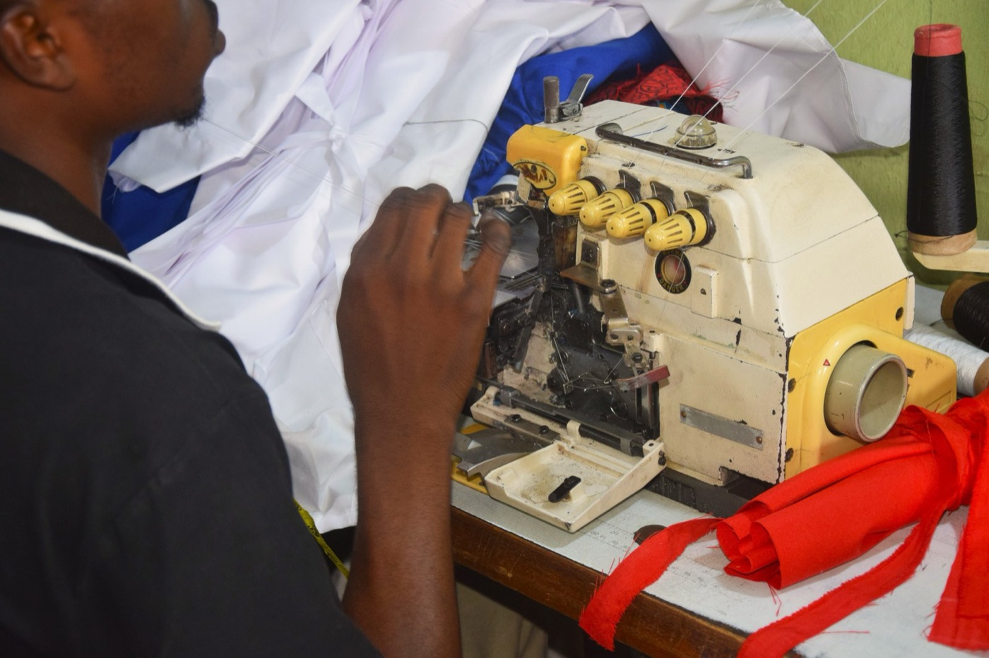 Sewing polyester in a garment factory. The fibre's water is behind it, in a refinery; its plastic is ahead of it, in every wash.