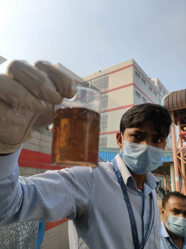 An engineer holds up a beaker of water outside a textile plant