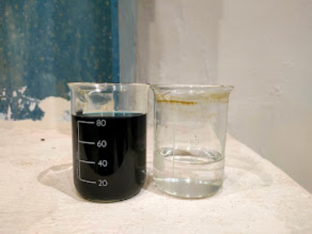 One beaker of black water beside a beaker of clear water