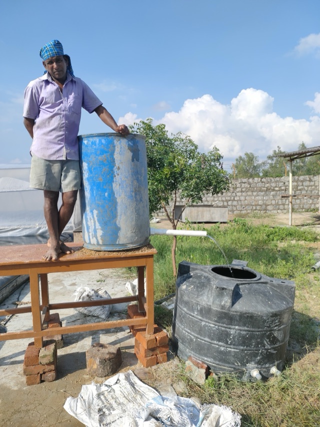 A man standing beside a simple sand filter feeding a tank
